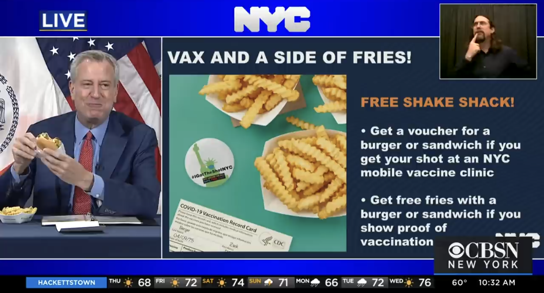screen capture of CBSN News showing Bill de Blasio, 
mayor of New York City holding a burger with a smug face. A transacription of the text beside 
him reads:
VAX AND A SIDE OF FRIES
FREE SHAKE SNACK!
Get a voucher for a burger or sandwich if you get your shot at an NYX mobile vaccine clinic
Get free fries with a burger or sandwich if you show proof of vaccination
CBSN NEW YORK
